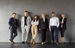 © Studio Romantic - Full length portrait of confident business people men and women looking at camera and smiling on dark gray background. Company employees group in formal clothes standing in office confidently.