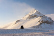 © Travel 'n' Lifestyle - View of snowy mountain peak piercing the bright sky, while a solitary figure sits on the snow-covered ground, bathed in the soft light, Snefellsnes, Eyja- og Miklaholtshreppur, Iceland.