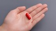 © suyu - Female hand holding a single capsule on gray background, symbolizing healthcare, medicine, treatment, and simple solution concept for wellness, supplement or medical therapy