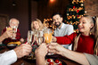 © deagreez - Family Christmas celebration with toasting glasses around a festive dinner in a cozy home interior featuring a decorated tree and warm lights creating a joyful winter mood