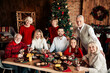 © deagreez - Family gathers for Christmas dinner around a festively set table with a tree and decorations in a cozy home celebrating the winter season