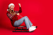 © deagreez - Funny festive sled ride girl in red sweater with santa hat on bright christmas backdrop merry holiday vibe