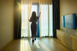© shine - Beautiful young woman opening curtains and stretching after wake up in living room. Awake woman wake up in morning and feeling fresh, enjoying view of sunrise. Good morning, new day, weekend, holiday.