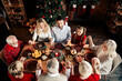 © deagreez - Family Christmas dinner around a cozy festive table with a decorated tree and warm lights indoors
