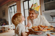 © Halfpoint - Grandmother in paper crown receiving kiss from grandchild.