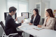© Tj - Business team members are analyzing financial data and charts on a clipboard and computer screens during a professional meeting in a modern office, focusing on collaboration and strategic planning