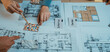 © InfiniteFlow - Hands of designers actively engaging in a collaborative session to select color swatches and analyze architectural plans on the table for an interior design project. SACTR