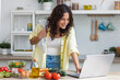 © nenetus - Healthy young woman cutting fresh vegetables and using laptop to recipes in the kitchen at home.