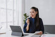 © amnaj - Asian businesswoman analyzing financial data on tablet, calculating numbers, expressing happiness and success at her office desk