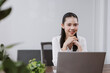 © amnaj - Young Asian businesswoman smiling and looking to camera, professional woman sitting at office desk, using laptop, feeling confident