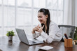 © amnaj - Young Asian woman working from home, smiling and communicating during an online video conference on her laptop