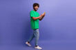 © deagreez - Young man in casual green t-shirt holding smartphone cheerful and smiling against purple background conveying positivity
