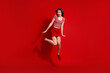 © deagreez - Young brunette woman jumping playfully against a vibrant red background in casual red attire showcasing cheerful energy