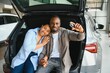 © Serhii - Happy african american couple showing car keys sitting in trunk at dealership