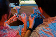 © InfiniteFlow - Cropped of hands couple with joysticks sitting sofa playing video game together at back side view with fronted snack and drinks with fun mood at neon light color living room at modern home. Infobahn.