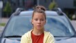 © Vlad - Camera moving back from pretty teenage girl standing outdoors near car in city looking at camera with serious face expression. Caucasian teen kid in street at vehicle. Close up