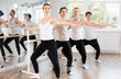 © JackF - Active dancing young women and guys engaged in group classes in studio perform demi plie pose near ballet barre in modern gym