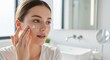 © Running opossum - young caucasian woman applying face cream in a bright bathroom, morning skincare routine