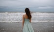 © simba kim - young girl in a light green dress standing on a flooded beach, stormy ocean waves crashing behind her, overcast cloudy sky