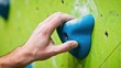 © K silver - Closeup of a climbers hand gripping a blue climbing hold on a textured green wall, showcasing strength and determination in indoor rock climbing