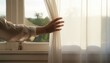 © Swan - Woman's hand opening a sheer curtain to let in the bright morning sunlight, symbolizing hope, peace, and a new beginning.