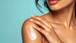 © Ramavanjava - A woman applies moisturizing cream to her shoulder, showcasing smooth skin against a blue background.