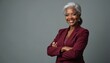 © Viktor - Stylish confident mature black woman stands in maroon business suit. Smiles with arms crossed. Strong female business leader represents success, power, pro achievement in studio isolated portrait.