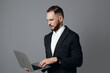 © SHOTPRIME STUDIO - A focused professional man in a dark suit uses a laptop against an isolated gray background, conveying confidence, concentration, and business readiness.
