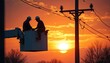 © Viktor - Two utility workers in bucket truck fix power lines at sunset. Wear hard hats, working high up on electric pole against vibrant orange sky. Dedicated crew ensures energy flow for community safety.