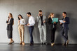 © Studio Romantic - Full length portrait of business people men and women in formal clothes talking on a meeting indoors. Company employees team standing in a row on gray wall background communicating with each other.