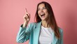 © Viktor - Laughing girl points finger up, gets bright idea. Woman in aqua jacket poses in studio. Brainstorm presentation with joyful student at pink backdrop. Positive model looks happy, excited and cheerful.