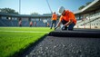 © Maryna - Workers install new artificial turf on football field. Stadium under renovation with grass replacement. Sport arena maintenance with modern tech. Construction team works for new event season