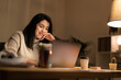 © Studio Marmellata - Positive young Arab woman in casual sweater sitting at table with laptop and making a video call on project during evening time
