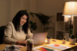 © Studio Marmellata - Positive young Arab woman in casual sweater sitting at table with laptop and making a video call on project during evening time