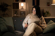 © Studio Marmellata - Concentrated Arab female in casual beige outfit and eyeglasses sitting on sofa with documents using laptop while working online at home