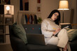 © Studio Marmellata - Concentrated Arab female in casual beige outfit and eyeglasses sitting on sofa with documents using laptop while working online at home