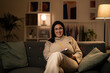 © Studio Marmellata - Smiling female in casual clothes and eyeglasses sitting on gray couch with laptop and pencil in living room looking at camera