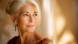 © Sawat - Thoughtful mature woman with silver hair gazes out a window, showcasing natural beauty and serene expression in warm, soft lighting and cozy environment
