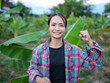 © buraratn - Empowered woman smiling confidently in lush green field, showcasing strength and positivity. vibrant banana leaves create lively backdrop, enhancing uplifting atmosphere