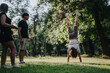 © qunica.com - Young adults spending leisure time in a scenic park, with one performing a handstand. The lush greenery and natural sunlight create a carefree and lively atmosphere of fun and friendship.