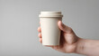 © utaem2022 - Hand holding a plain disposable coffee cup against a neutral background with soft lighting