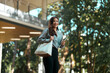 © Parichat - Young woman walking carrying tote bag and laptop