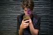 © Connect Images - A teenager is focused on looking at a smartphone against a textured stone wall. Munich, Germany