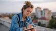 © Kliapko_Photo - Dreamy teenage girl in denim jacket, sketching in a notebook while sitting on a rooftop overlooking the city at sunset. Inspiration and youth concept, copy space.