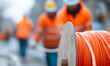© Alexey - Reel with orange fiber optic cable for fast internet connection with blurry men working in background. Telecommunications network infrastructure.