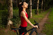 © Anastasia.photoyoga - Sport woman in sporty red clothes riding on bike in summer sunny day on the rural path near the trees. Healthy fit athlete body. Closeup sport portrait