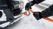 © velikiyzayats - Person in black gloves attaching a bright orange towing strap with a metal hook to the front bumper of a black car stuck in deep winter snow.