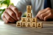 © Worrapol - Organization on the Rise: A focused professional meticulously arranges a stack of wooden blocks, each etched with a silhouette, forming a pyramid that symbolizes growth and structure.