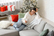 © Pixel-Shot - Beautiful young woman with mobile phone sitting on sofa in living room. Christmas celebration