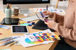 © Pixel-Shot - Young female designer working with graphics tablet and color samples at table in office, closeup